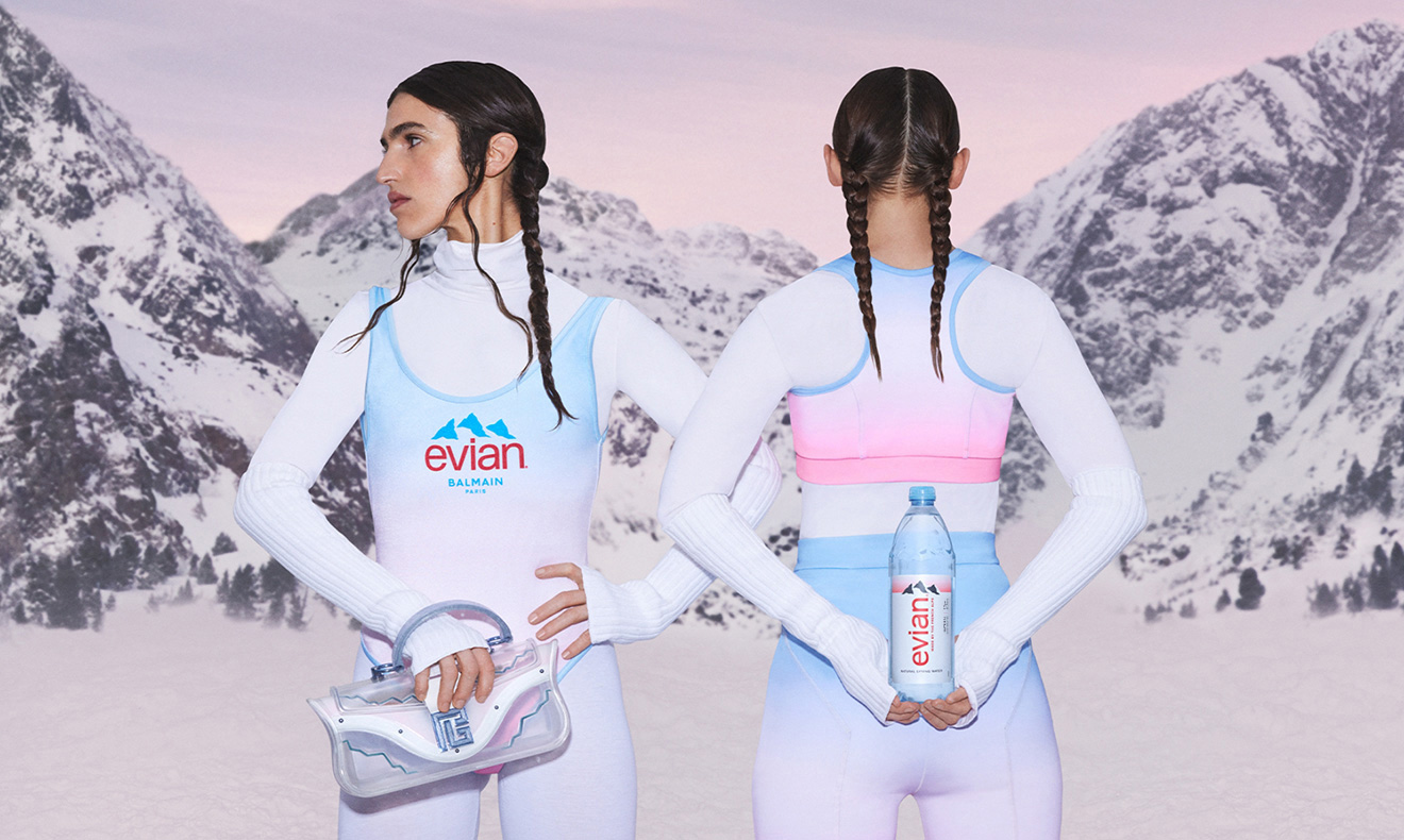 Two women posing in sportswear holding a handbag and water bottle from the evian and Balmain collection.