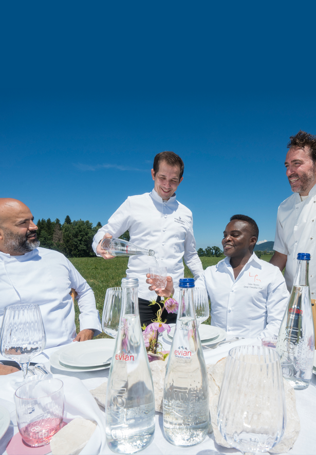 Four chefs at an outdoor table. One pours water.