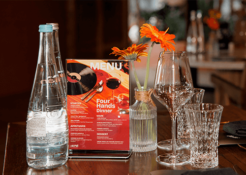 Table with "4 Hands Dining" Menu Card on table with evian® bottles.